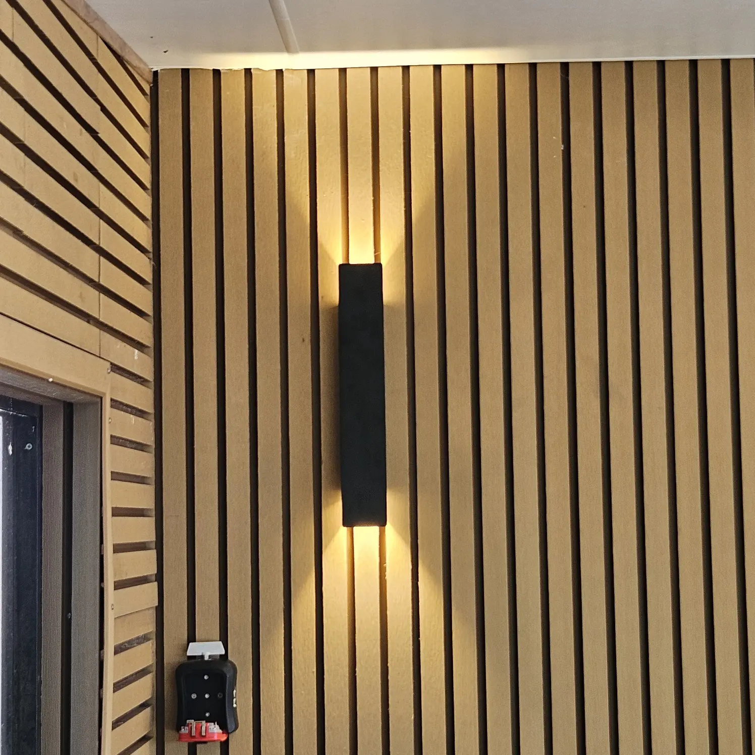 Black linear LED wall sconce casting warm light down a timber slat feature wall