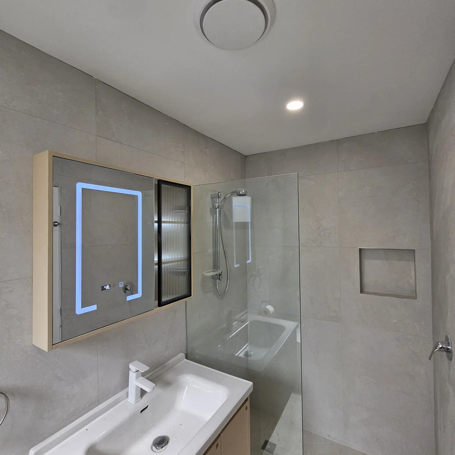 Bathroom vanity with illuminated LED mirror cabinet, ceiling fan light and downlight above the basin