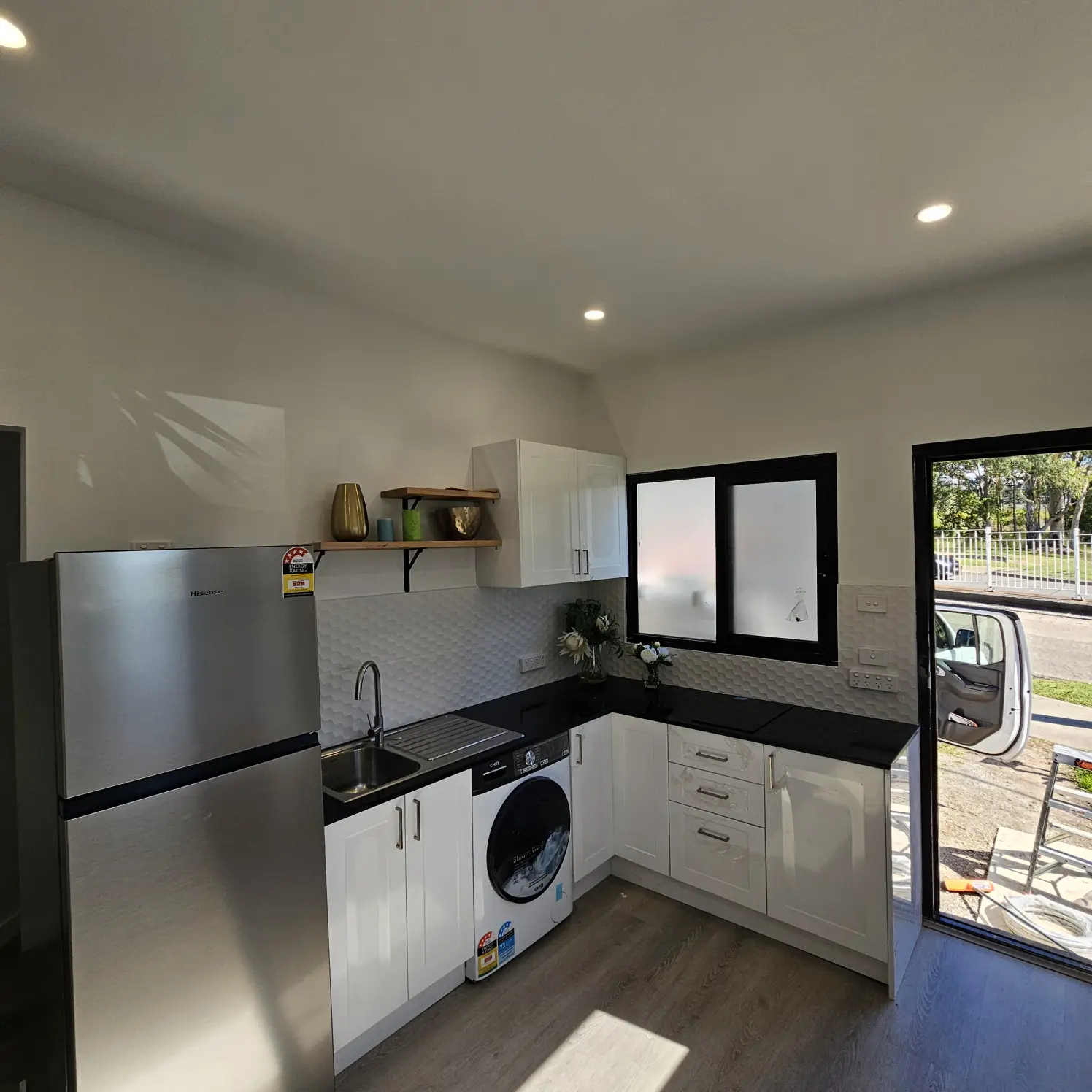 Compact kitchen with stainless steel fridge, washing machine and downlights above the benchtop and sink