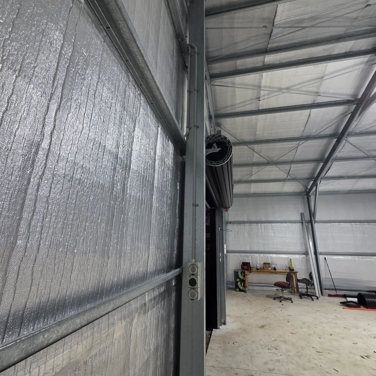 Insulated shed workshop with roller door, wall-mounted power points and light switches beside the frame