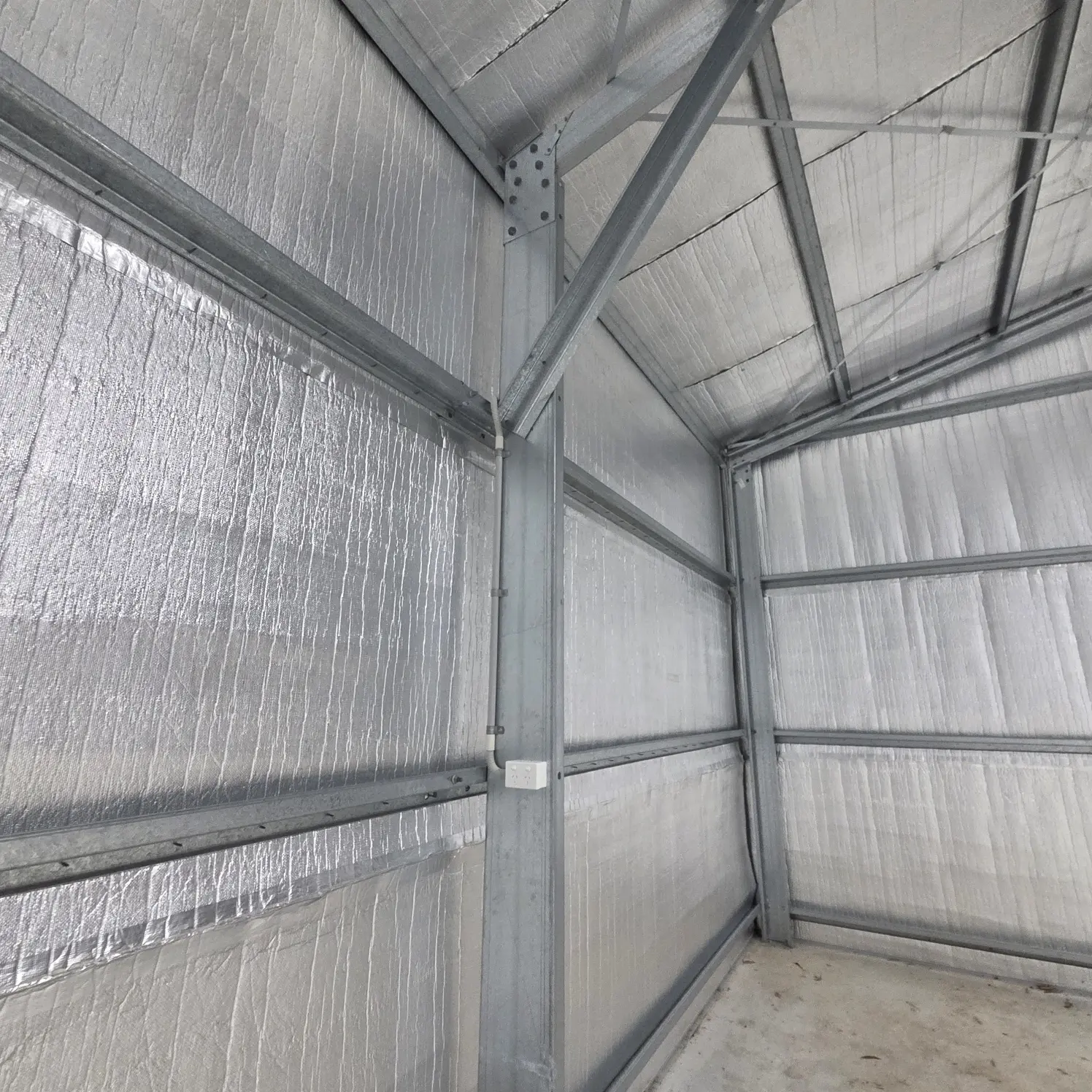 Foil-insulated shed interior showing conduit and cabling run neatly along the steel roof framing