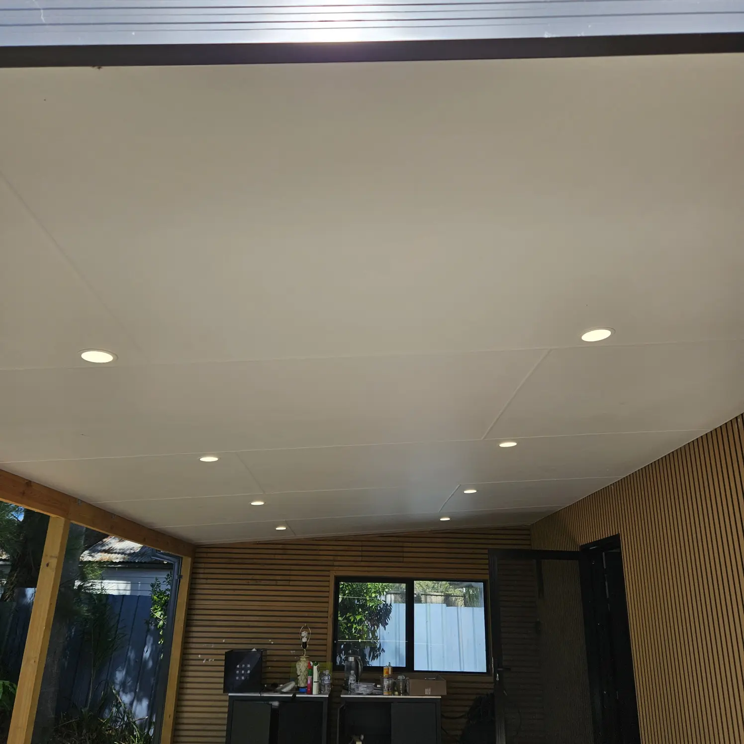 Covered outdoor patio with flush LED downlights across the ceiling and a timber slat feature wall