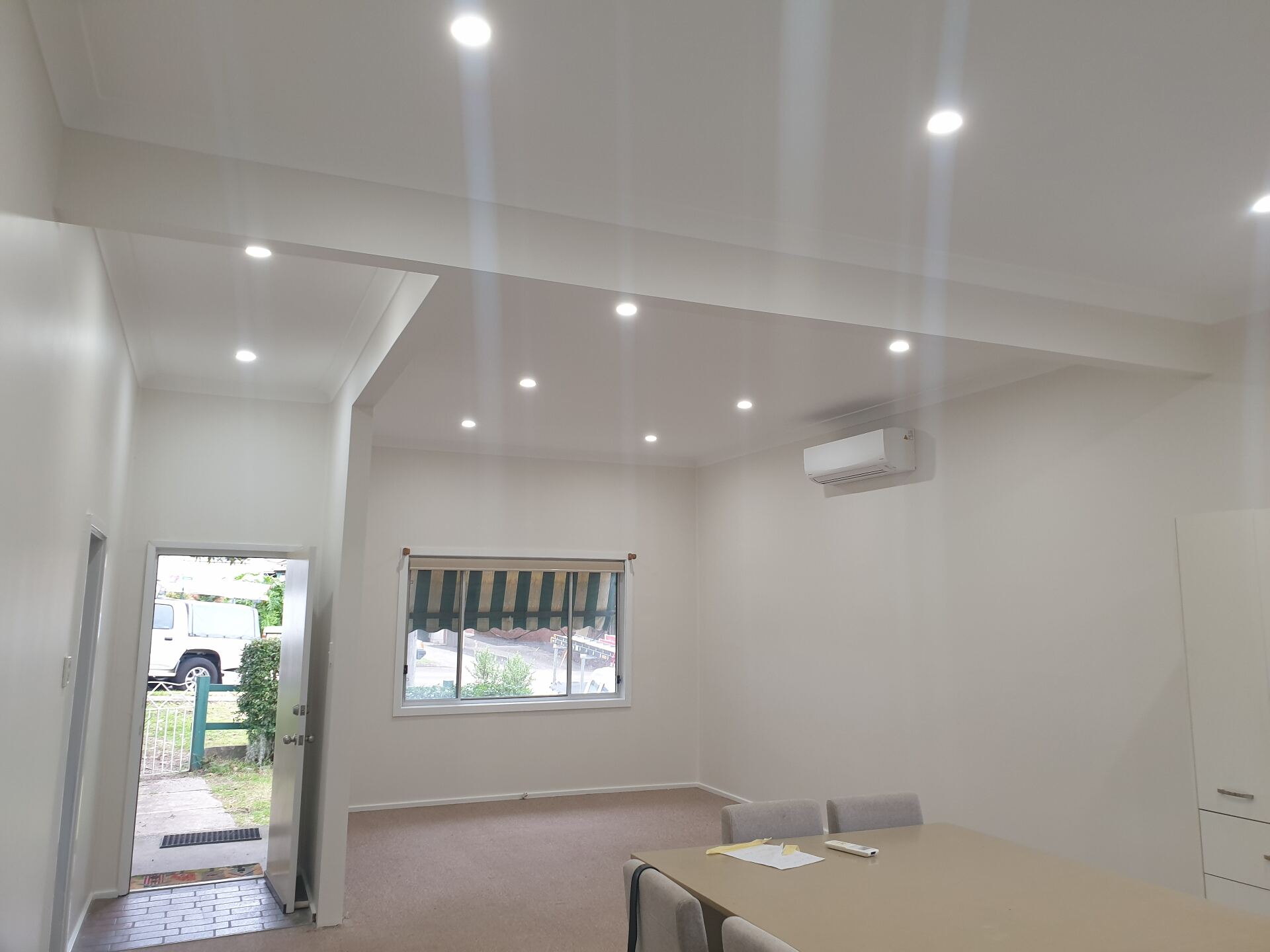 Freshly painted open-plan room with new LED downlights, a split-system air conditioner and a kitchen bench