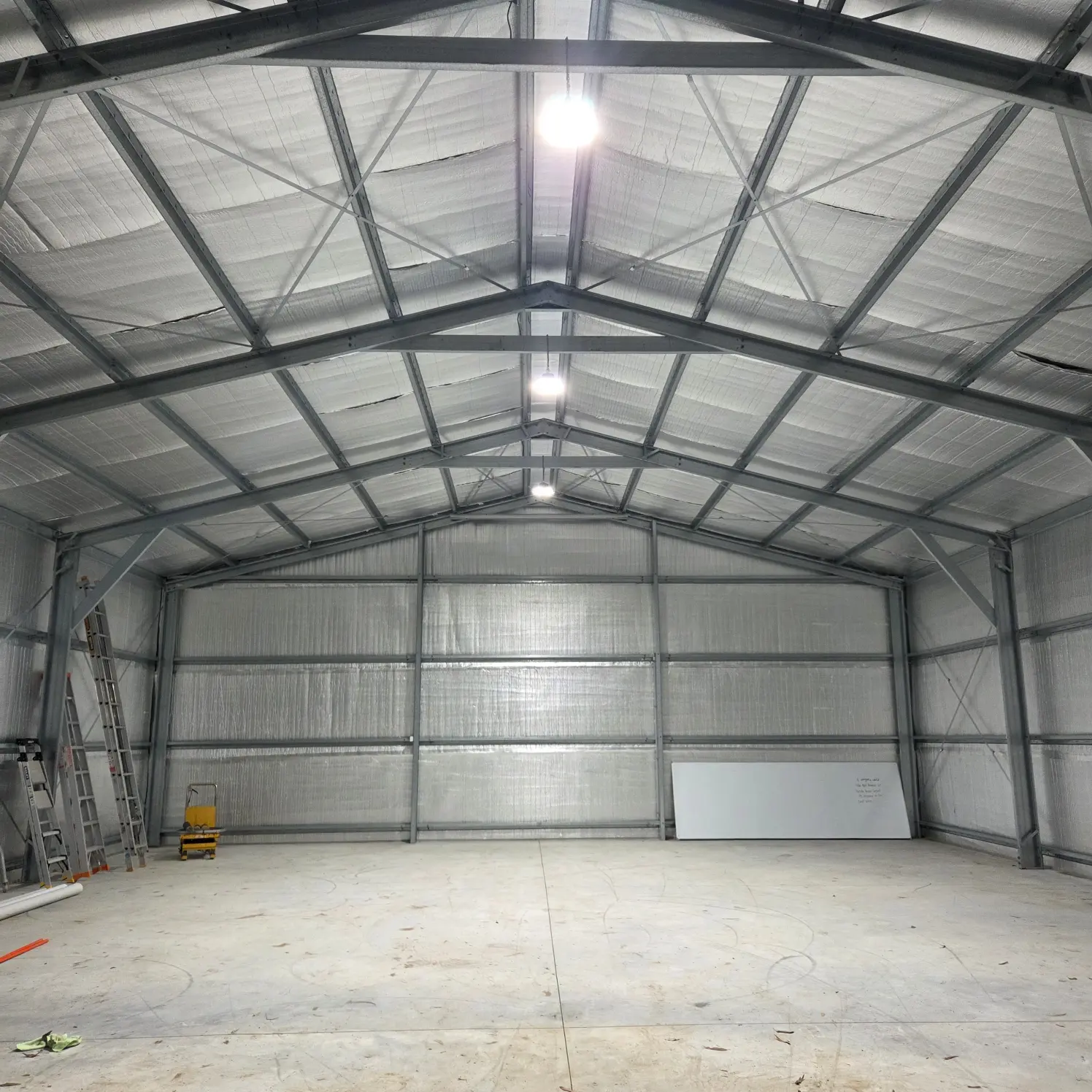 Interior of a large steel-framed shed lit by high-bay LED battens mounted along the roof trusses